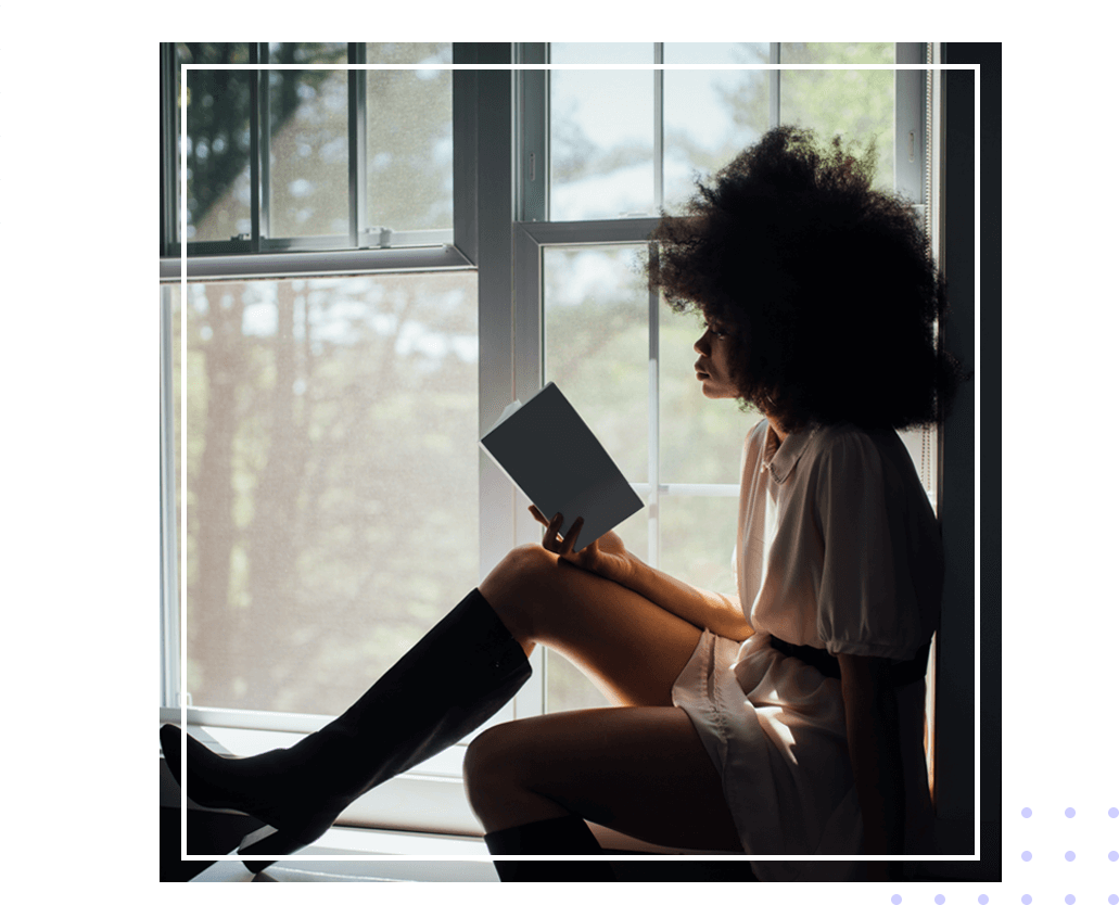 A woman sitting in front of a window reading.