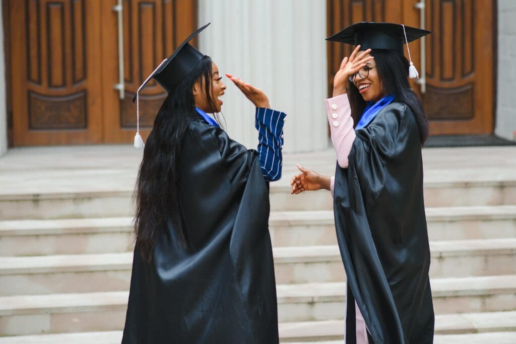 Two women in graduation gowns are standing outside.