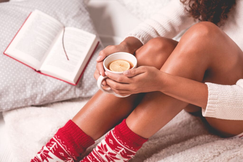 A woman sitting on the bed with her legs crossed holding a cup of coffee.