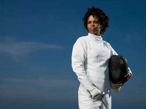 A woman in white holding a fencing mask.