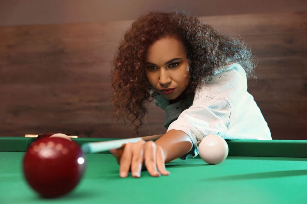 A woman leaning over to hit an apple on the pool table.