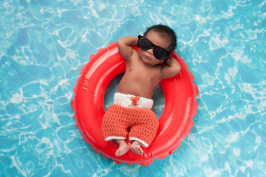 A baby wearing sunglasses and laying on an inner tube in the water.