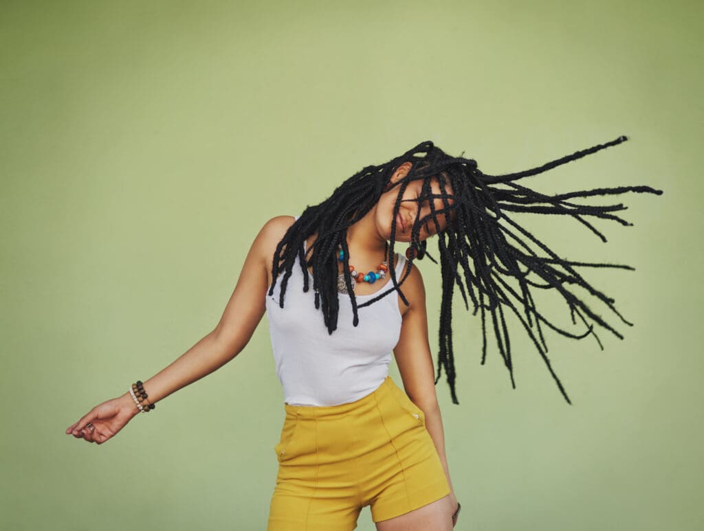 A woman with dreads is dancing in front of a green wall.
