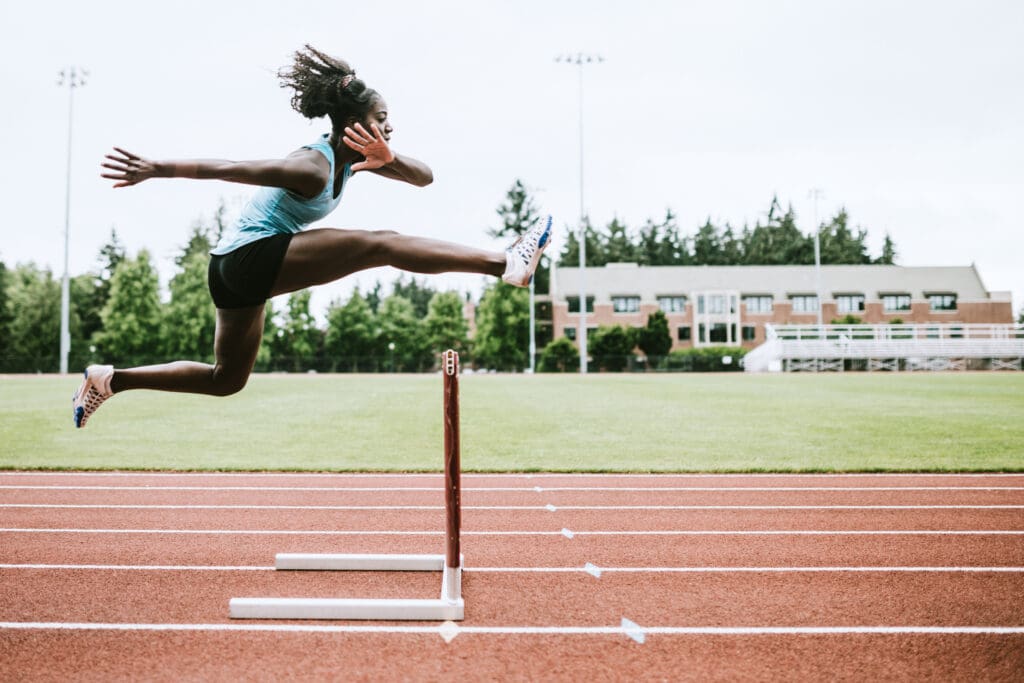 A woman jumping over an obstacle on a track.