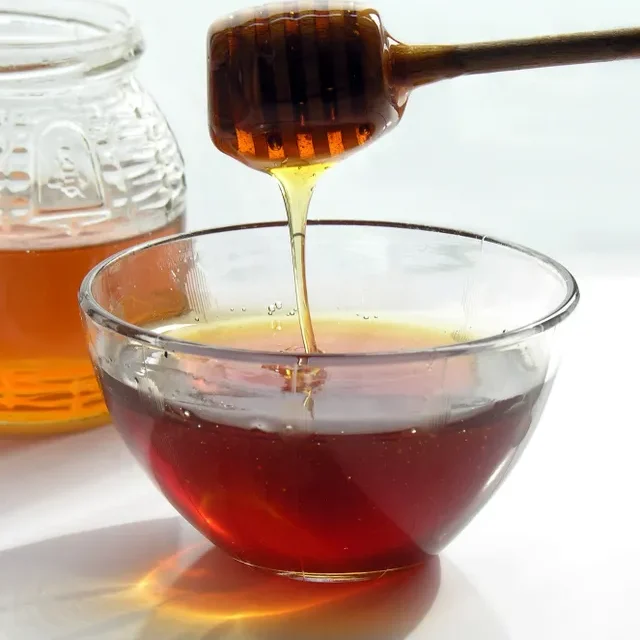 A honey dipper is being poured into a bowl of liquid.