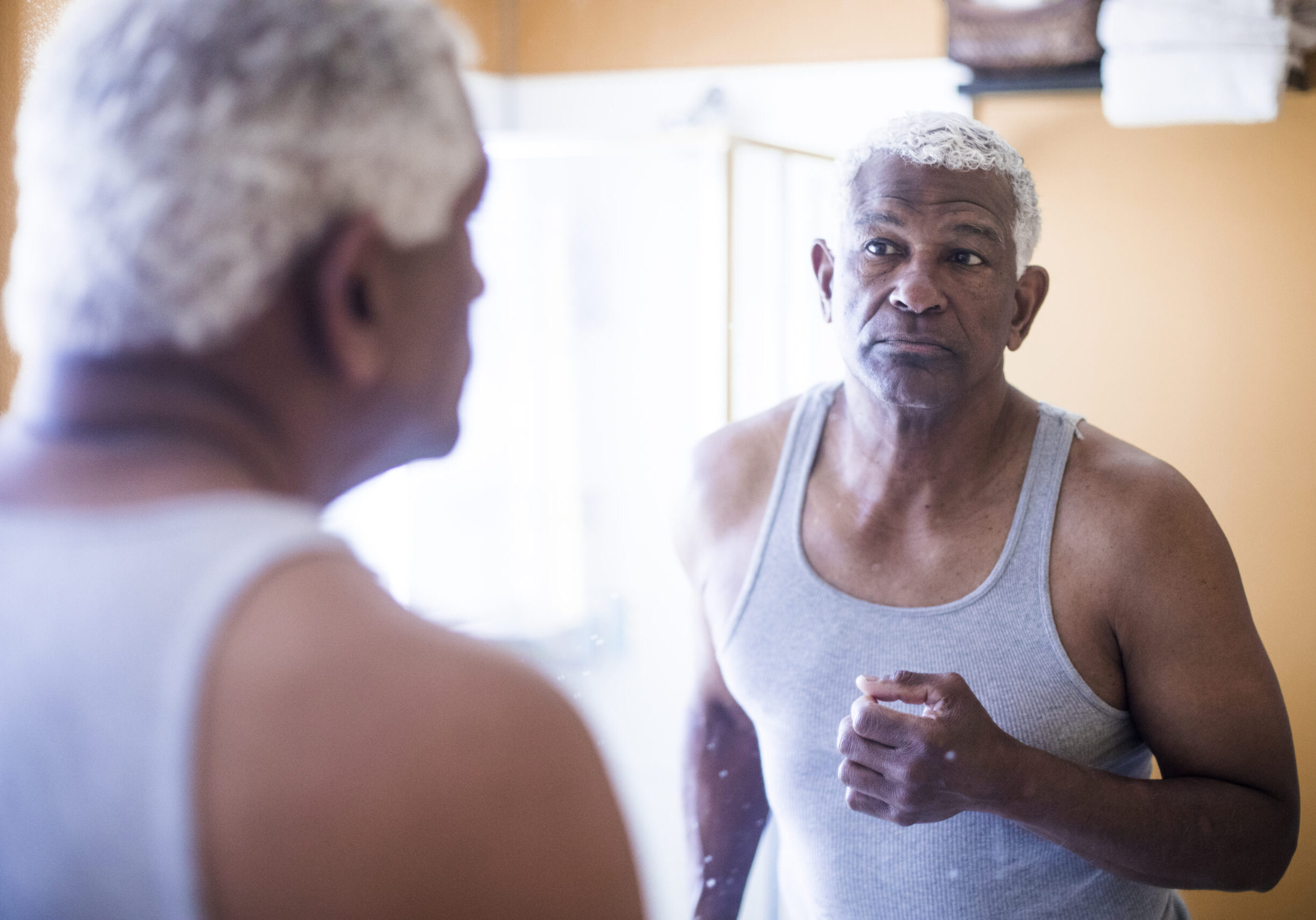 A senior black man looks at himself in the mirror in the bathroom