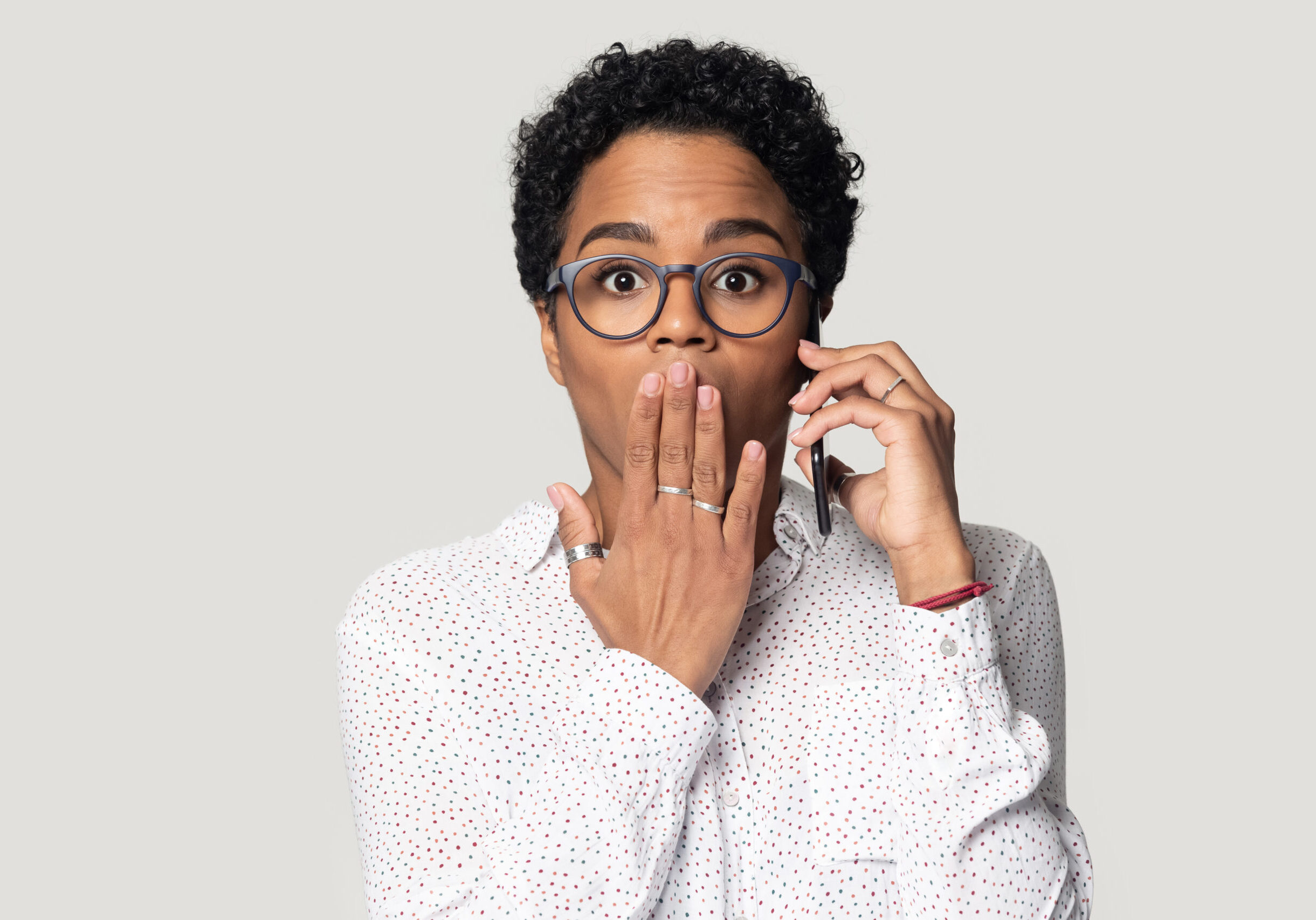 Shocked african American woman in glasses isolated on grey studio background get unexpected message talking on smartphones, stunned black female in spectacles speak on cell hear shocking news