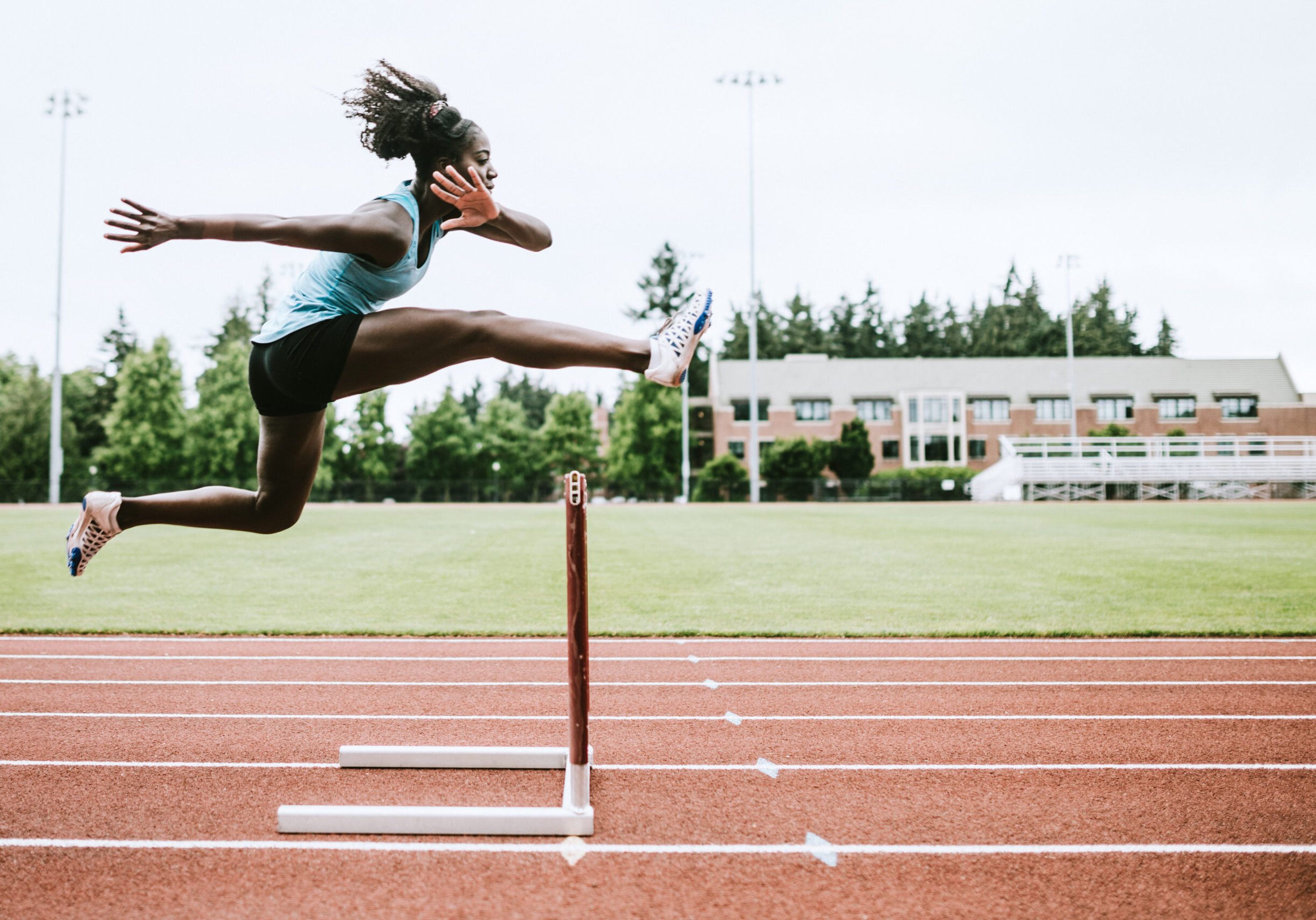 A young woman does hurdling training for her track competition training.  Captured mid- jump. Horizontal image with copy space.